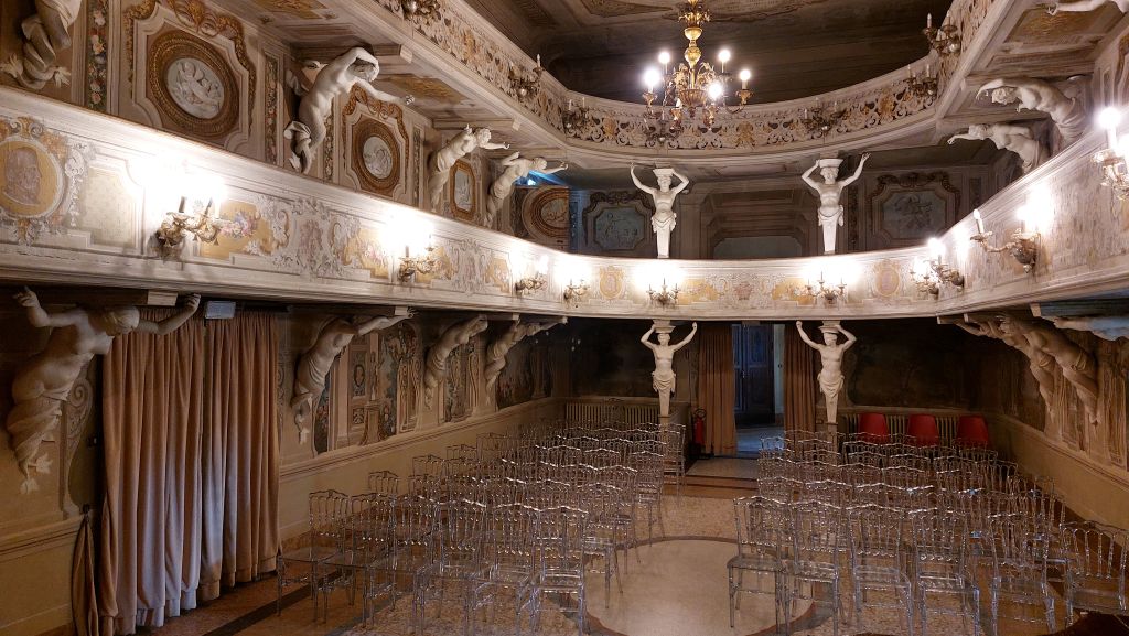 Interno di una sala decorata con statue e affreschi, con sedie trasparenti disposte ordinatamente per un evento.
