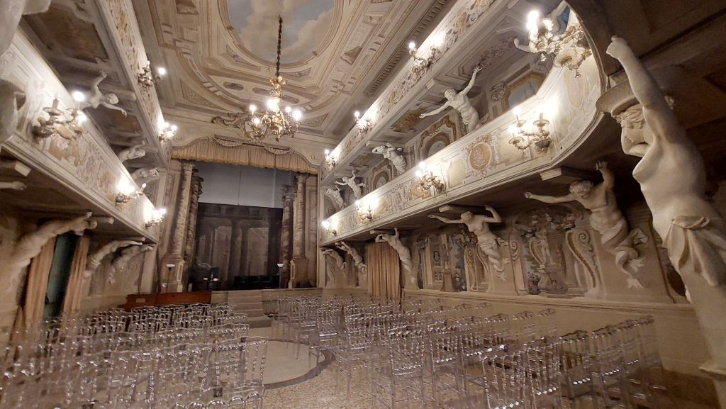Interno di una sala eventi con decorazioni elaborate, sculture e luci, vista da un'angolazione che mostra le sedie trasparenti disposte per un evento.
