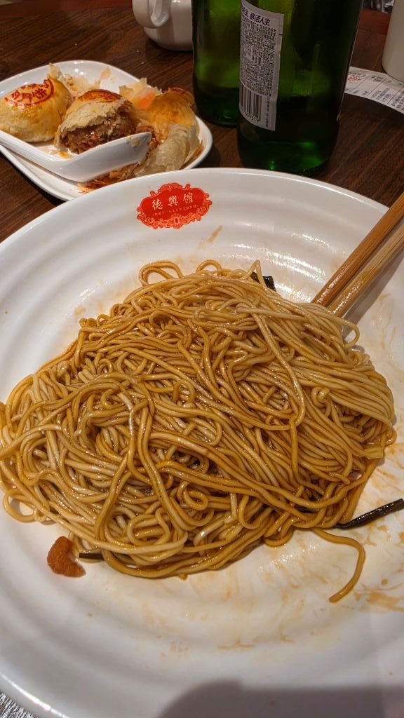 Un piatto di spaghetti cinesi con salsa, accompagnato da un piatto di antipasti e bottiglie di bevande sul tavolo.