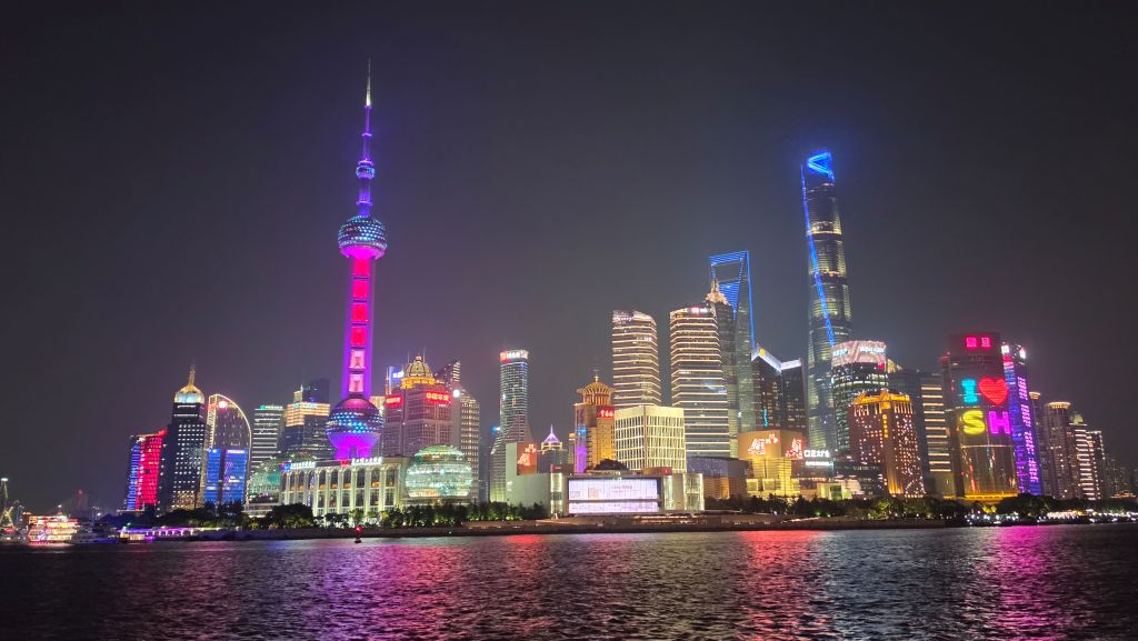 Vista notturna dello skyline di Shanghai illuminato, con la Torre di Shanghai e il Bund visibili.